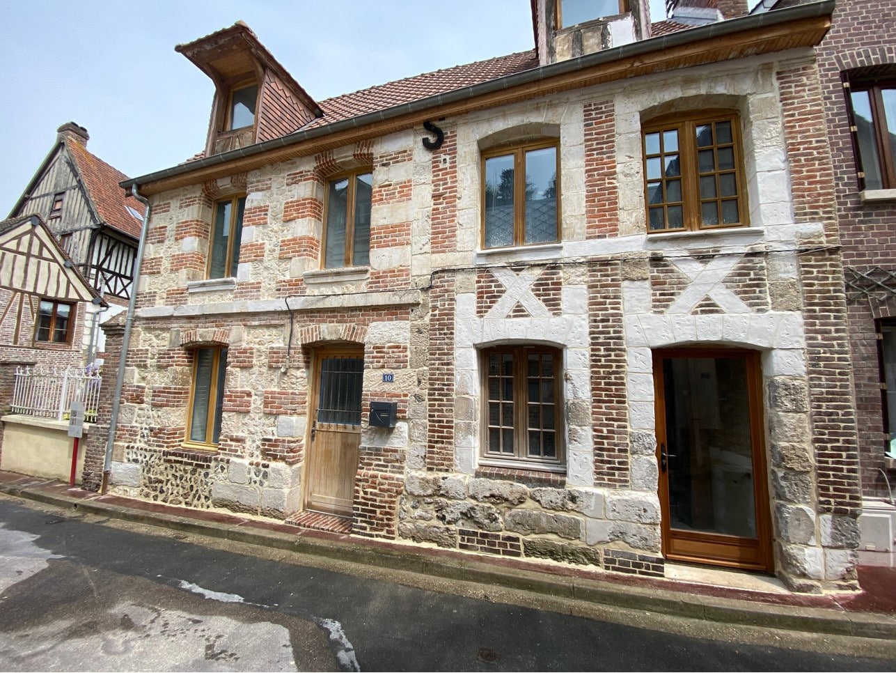 Façade d'une maison ancienne rénovée, avec des murs en pierres et briques, des fenêtres à cadre en bois et une porte en bois.